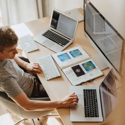 Chico sentado en un escritorio con múltiples laptops