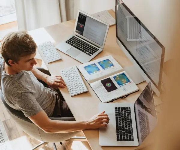Chico sentado en un escritorio con múltiples laptops